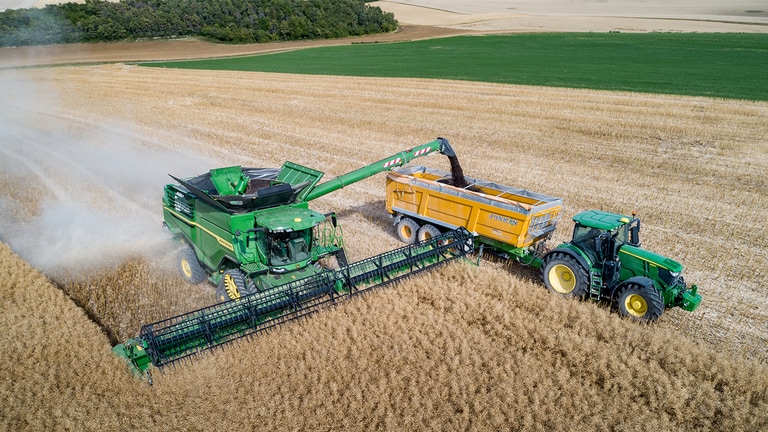 Der John Deere M&auml;hdrescher der X-Serie entl&auml;dt Raps in einen Kornwagen, der von einem John Deere-Traktor gezogen wird