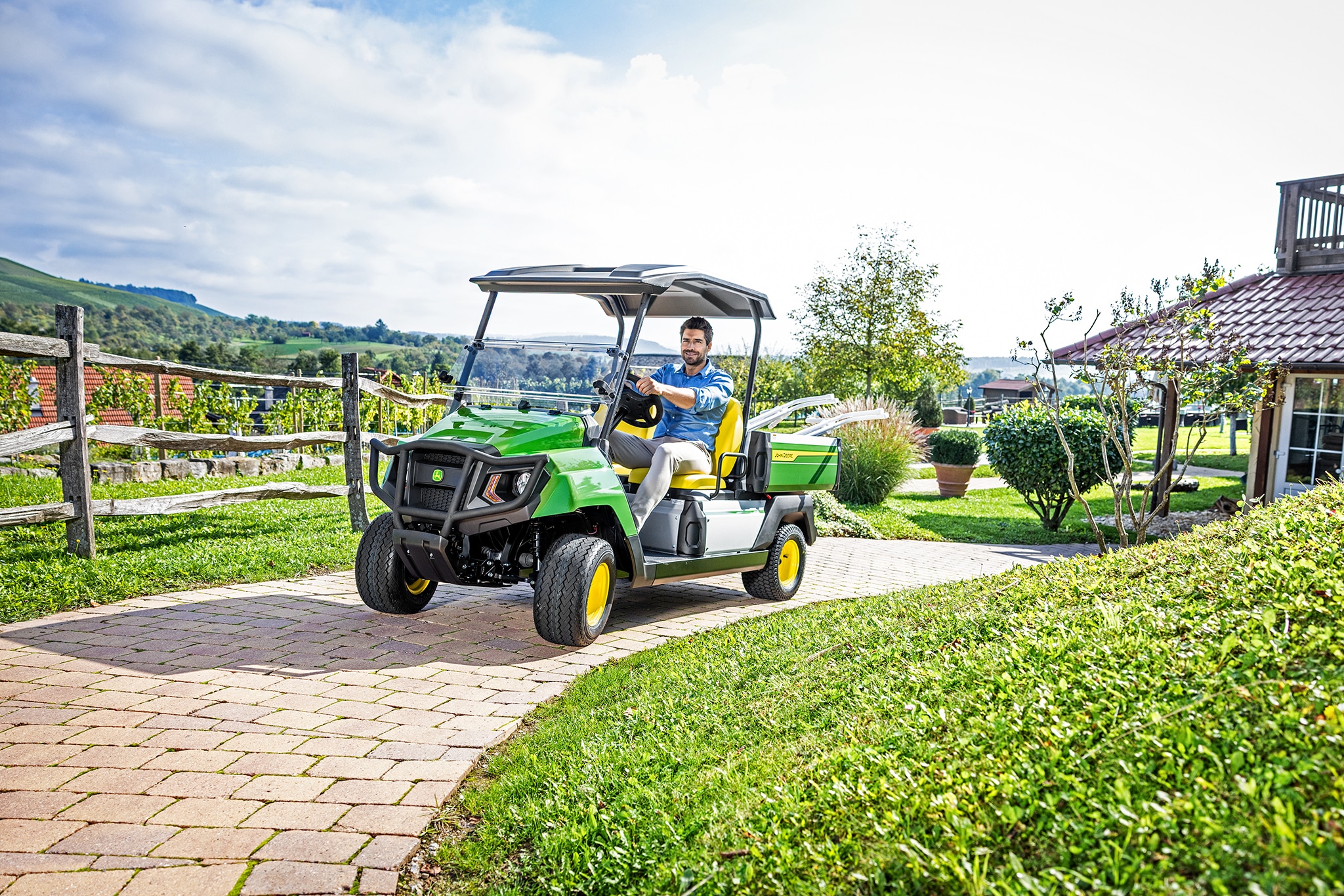 John Deere Gator GS beim Fahren in der Nähe eines Hauses auf einem befestigten Weg John Deere Gator GS beim Fahren in der Nähe eines Hauses auf einem befestigten Weg