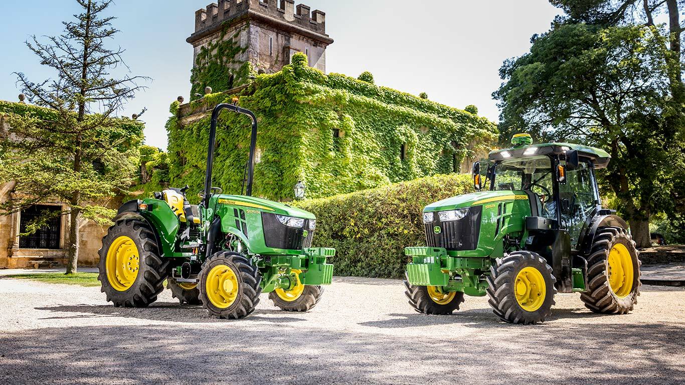 Grün-gelber John Deere Traktor 5075EN, der auf einem Feldweg durch einen Obstgarten fährt, umgeben von Obstbäumen und Sonnenlicht.