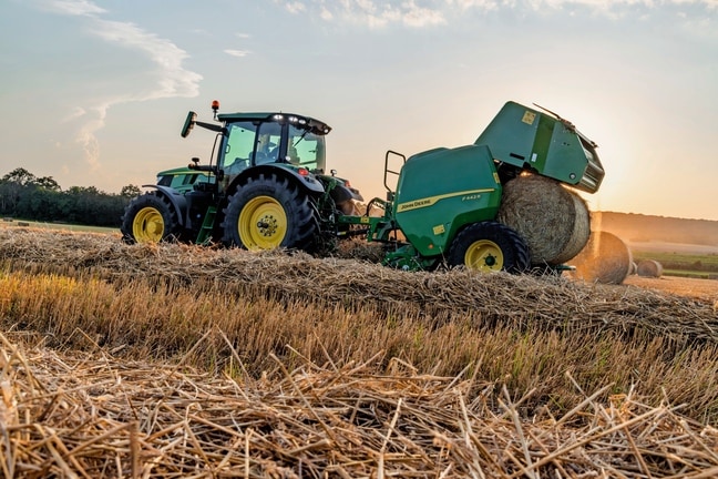 John Deere Ballenpresse F442M, gezogen von einem John Deere 6M Traktor, beim Auswerfen eines Strohballens