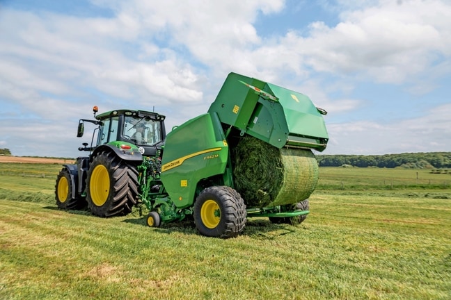 John Deere Ballenpresse F442M wird von einem John Deere Traktor 6M gezogen, der einen Grasballen abwirft