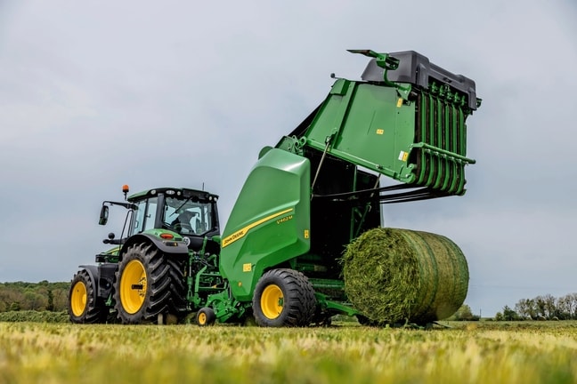 John Deere Ballenpresse V462M, gezogen von einem John Deere 6M Traktor, beim Auswerfen eines Grasballens