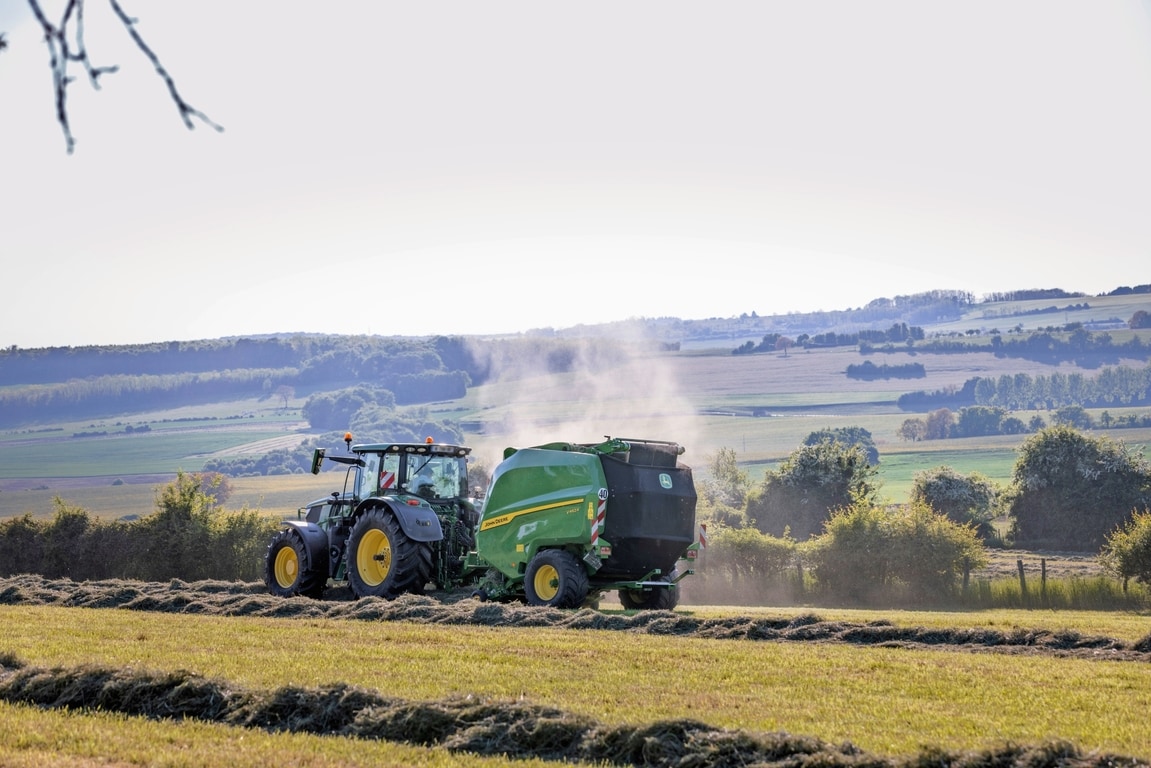 John Deere V462R, gezogen von einem John Deere 6R 185 Traktor, beim Heupressen