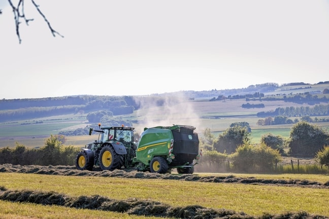 John Deere V462R, gezogen von einem John Deere 6R 185 Traktor, beim Heupressen