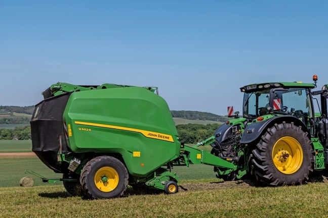 John Deere V462R, gezogen von einem John Deere 6R 185 Traktor, beim Heupressen